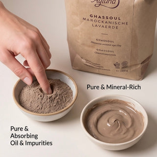 A hand presses into a mound of light brown powder in a small bowl, with a larger bowl of smooth powder and a kraft paper pouch labeled Agulfa Ghassoul shown on a clean light background. Text overlays read 'Pure & Mineral-Rich' and 'Pure & Absorbing Oil & Impurities'.