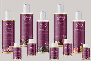 A collection of Ayluna haircare products, including various sizes of shampoo bottles and conditioner jars, arranged neatly against a solid light gray background. The packaging features a deep plum-purple color with white caps and gold accents.
